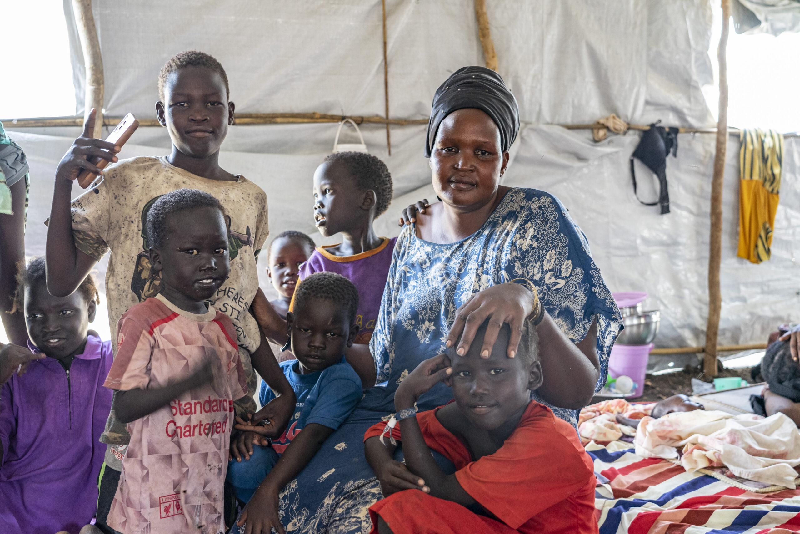 Batika, a refugee, poses for photo inside a tent in Renk with her children.