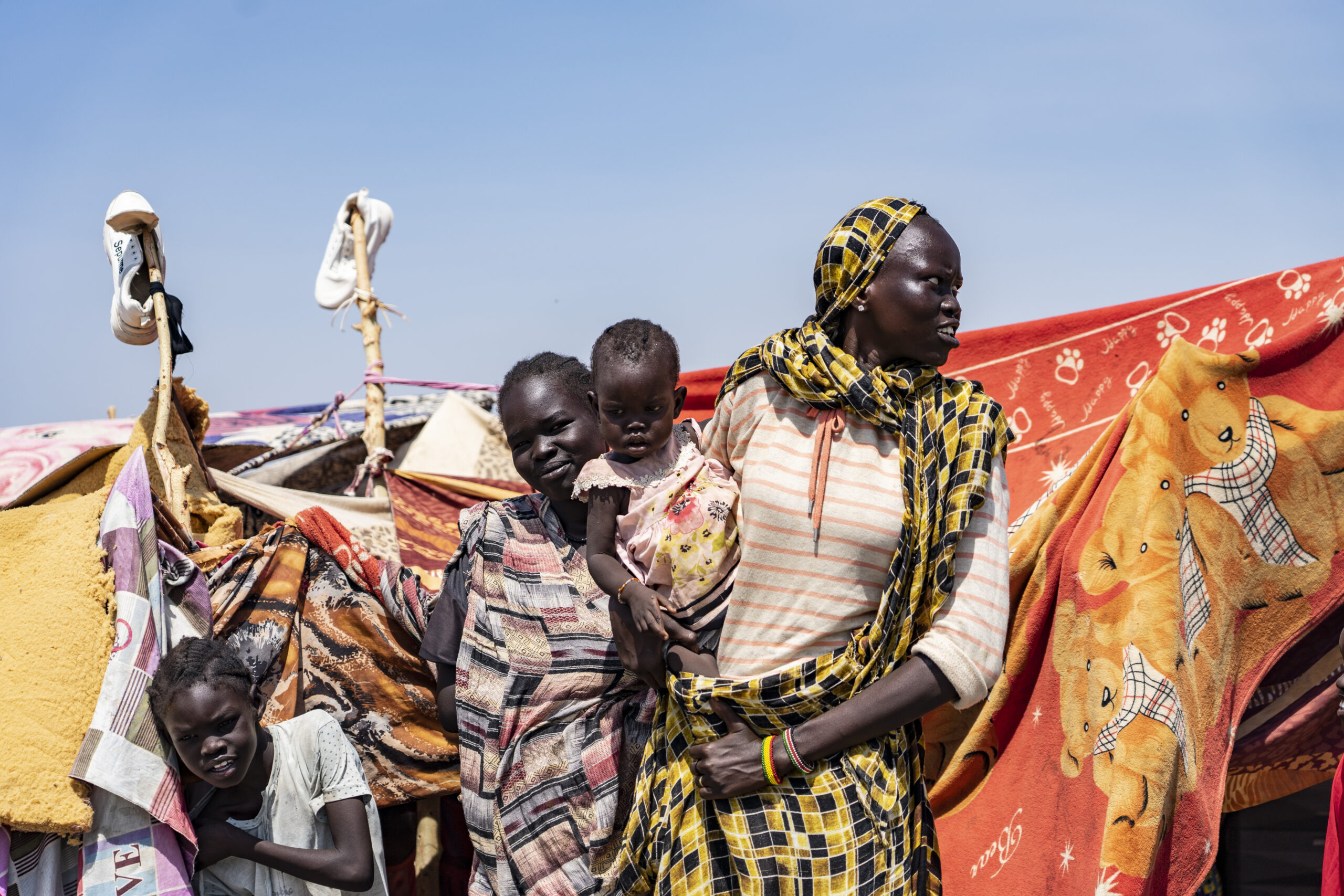 Refugee women hold baby outside their tent in refugee camp in Renk, South Sudan
