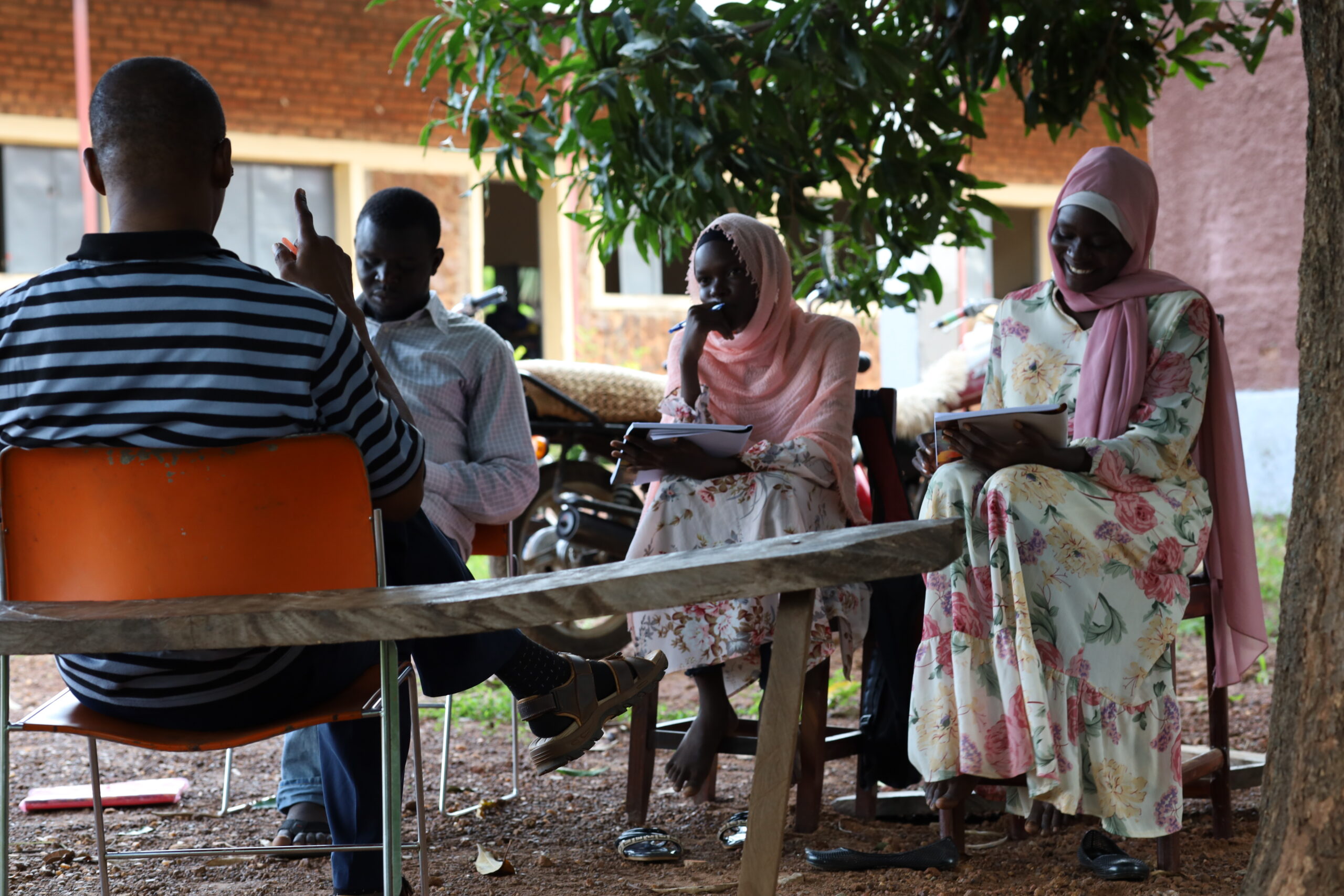 adults take literacy classes under the shade of a tree in South Sudan.