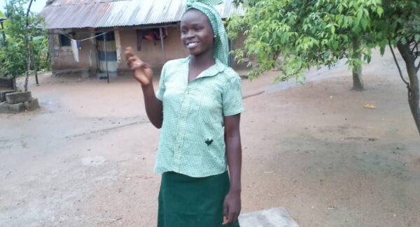 Agal stands outside her home smiling to the camera. She is in her school uniform.