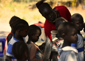 Teacher looks over students with chalkboards in an outdoor lesson.