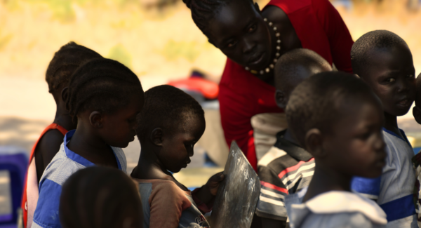 Teacher looks over students with chalkboards in an outdoor lesson.