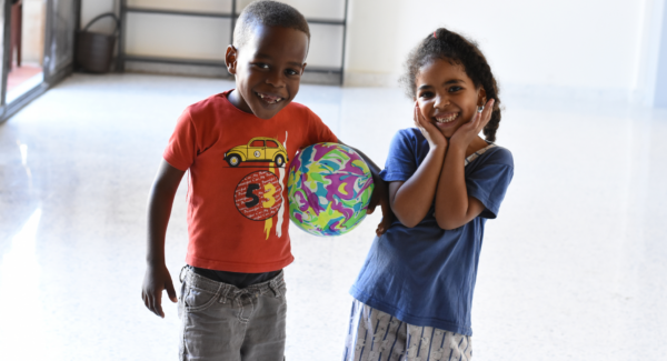 Migrant children smile to camera at Arrupe Migrant centre. they are playing with a ball.