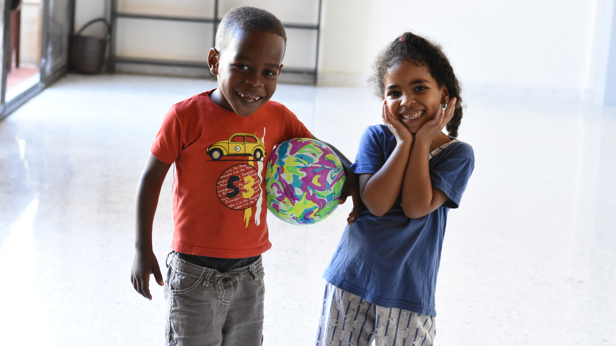 Migrant children smile to camera at Arrupe Migrant centre. they are playing with a ball.