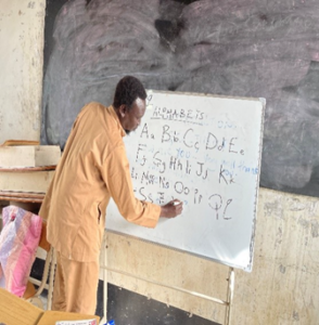 Muhktar, a teacher writes the English alphabet on a whiteboard. 