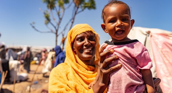 mother holds her toddler towards the camera. They're smiling