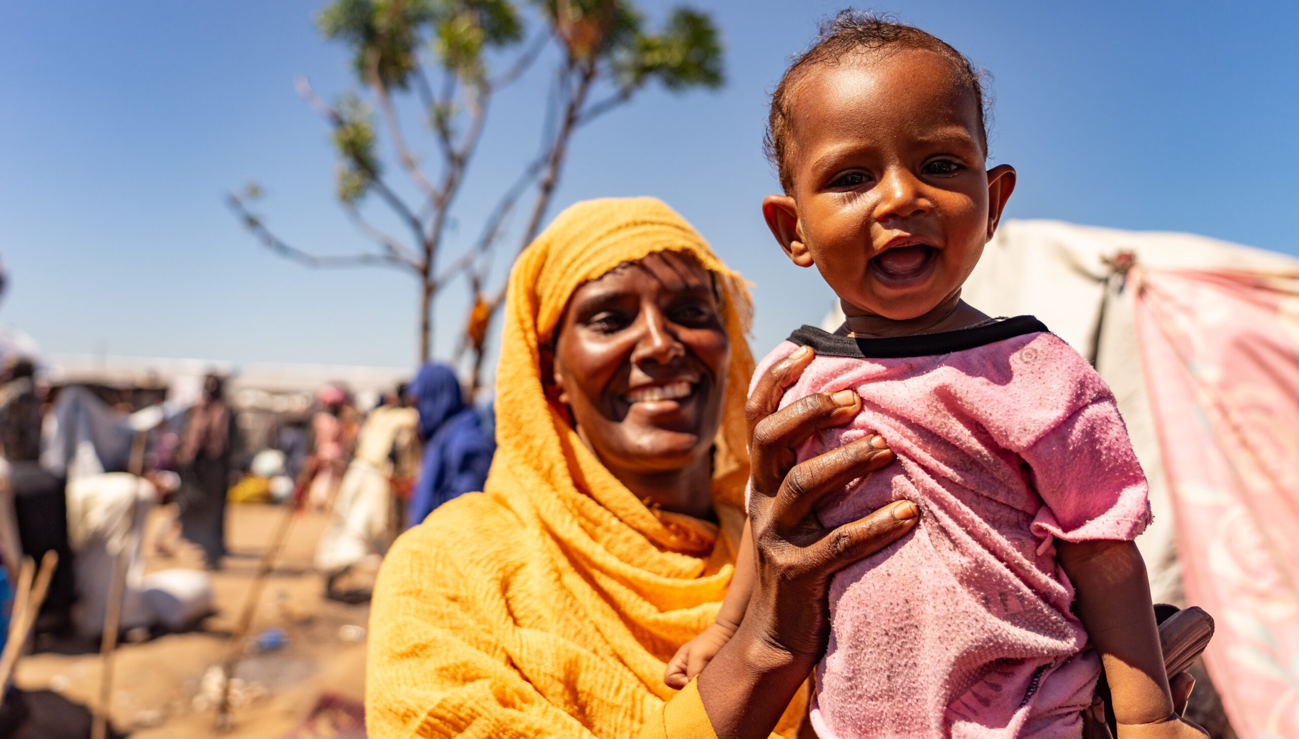 mother holds her toddler towards the camera. They're smiling